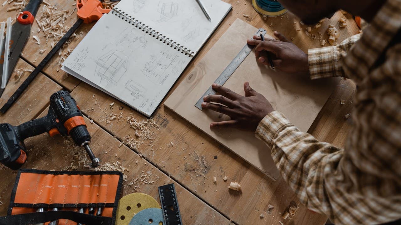 Hands over a sketch beside a drill on a workbench