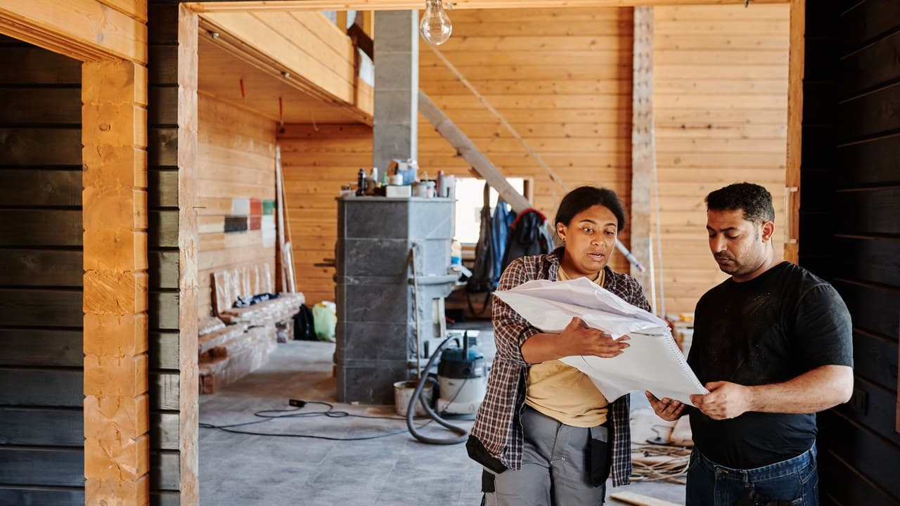 A tradesperson and a homeowner reading paperwork inside a house under renovation